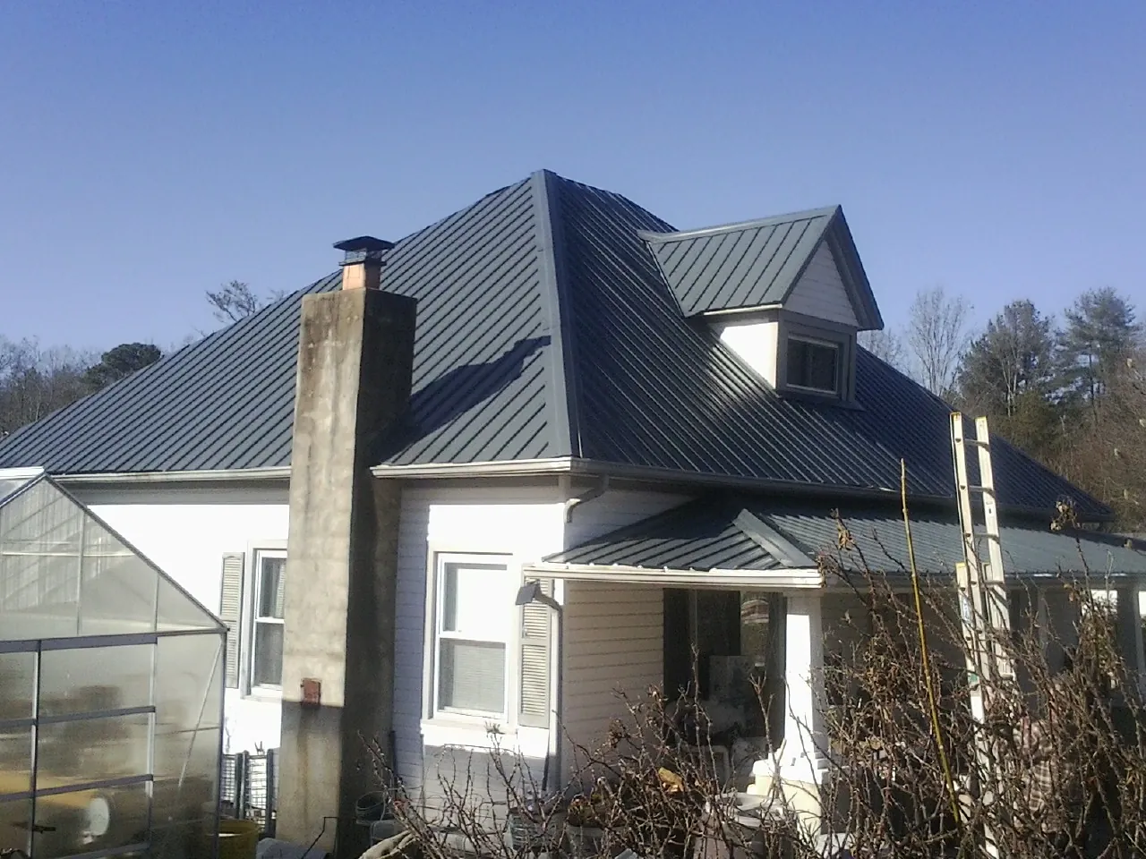 Dark blue standing seam metal roof on a white farmhouse with dormer — Slate & Tile Roof Repair by Roofing Brothers in Point Of Rocks