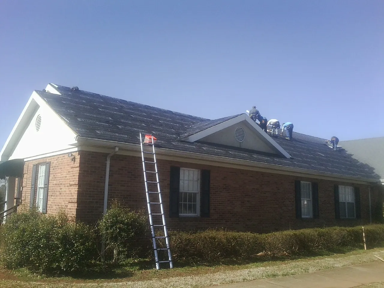 Crew tearing shingles off a brick ranch roof with a ladder set — Metal Roof Repair work by our crew in Point Of Rocks