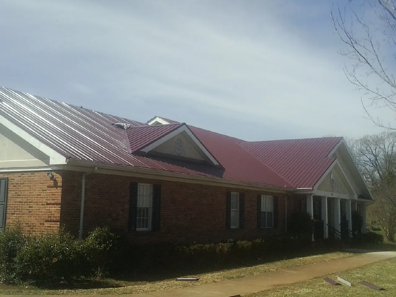 Red metal roof with gabled entries on a long brick building, from a Hail Damage Roof Repair job in Point Of Rocks