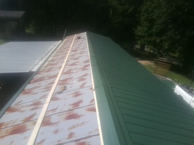 Old rusted panels beside newly installed green metal roofing — Wind Damage Roof Repair by Roofing Brothers in Point Of Rocks