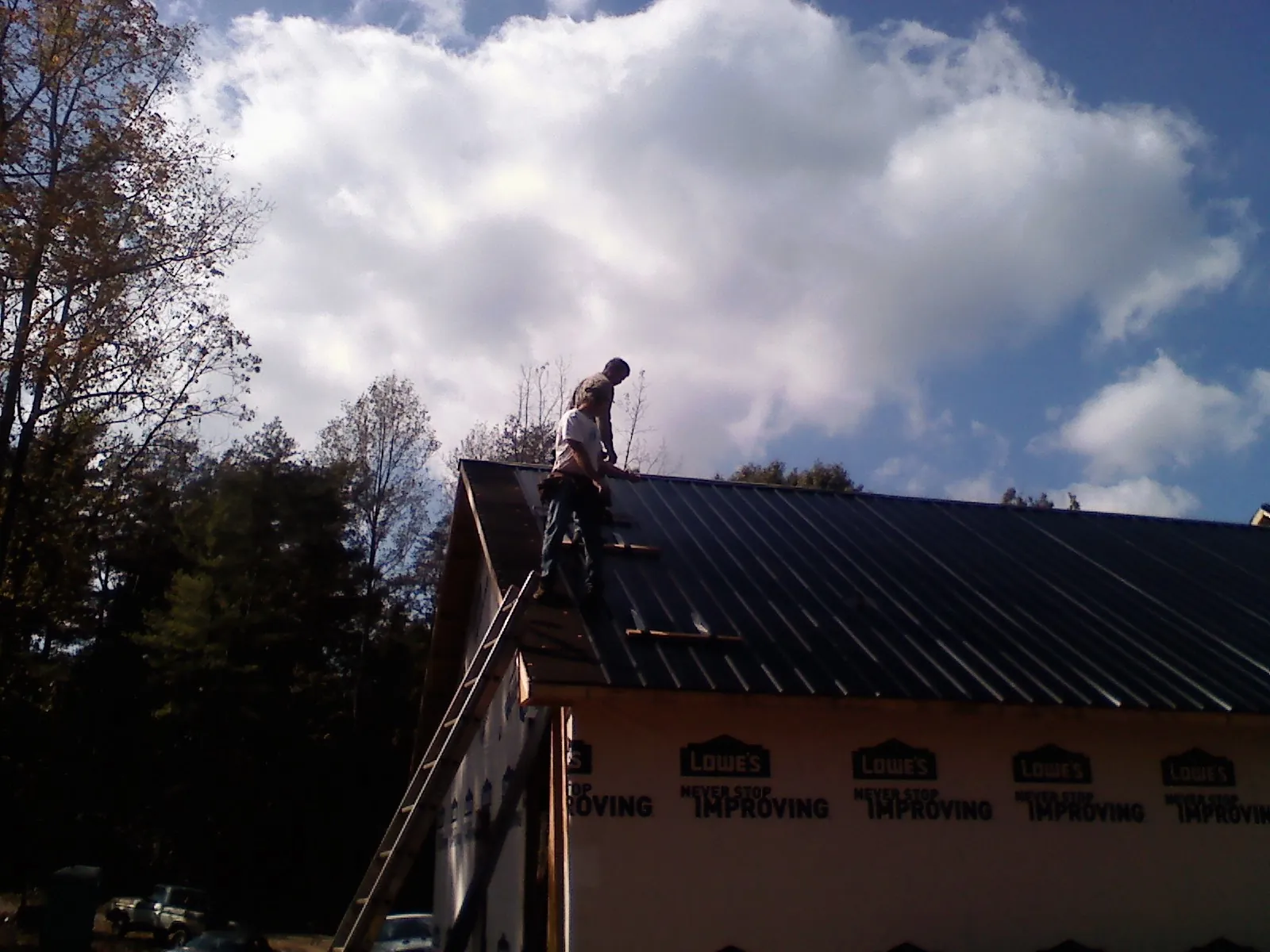 Roofer fastening dark metal panels high against a cloudy sky, from a Roof Inspection job in Point Of Rocks
