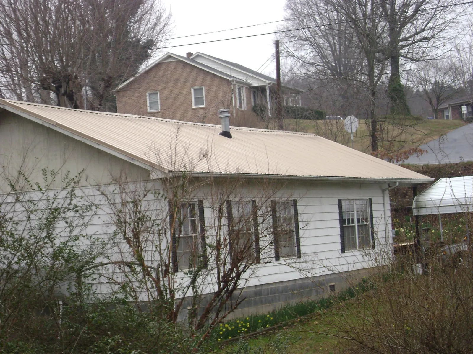 Tan metal roof on a white sided house set into a hillside — Commercial Roofing by Roofing Brothers in Point Of Rocks